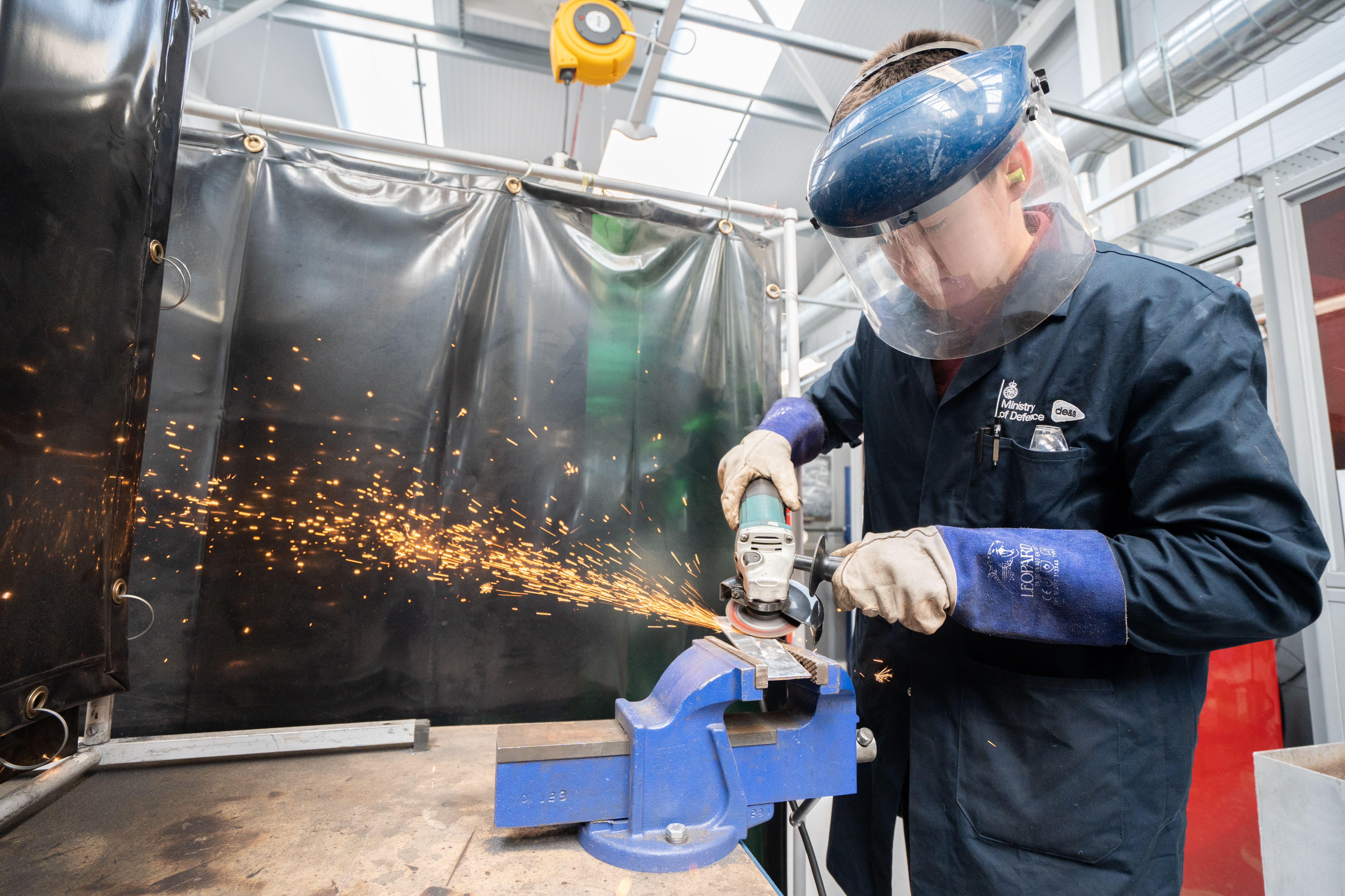 student wearing gloves and face mask using an angle grinder, sparks flying