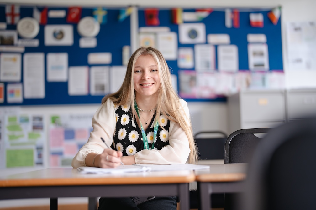 student in classroom writing, sitting at a desk