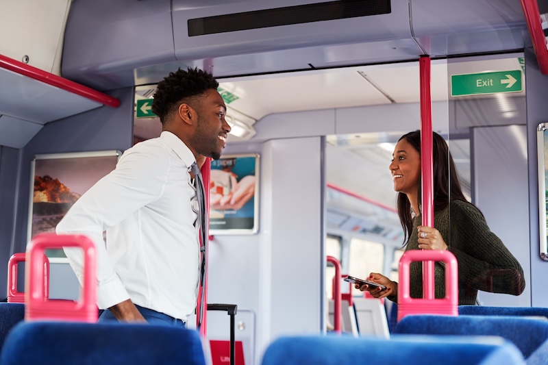Two people talking inside a train carriage with blue seats and red handrails