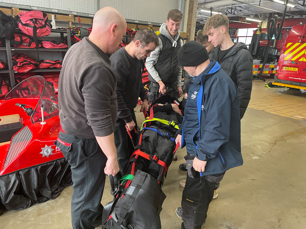 students picking up a stretcher with a student strapped in