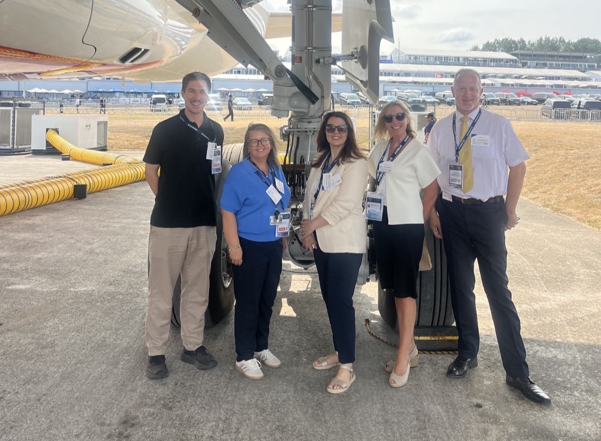 Stood posing and smiling in front of plane
