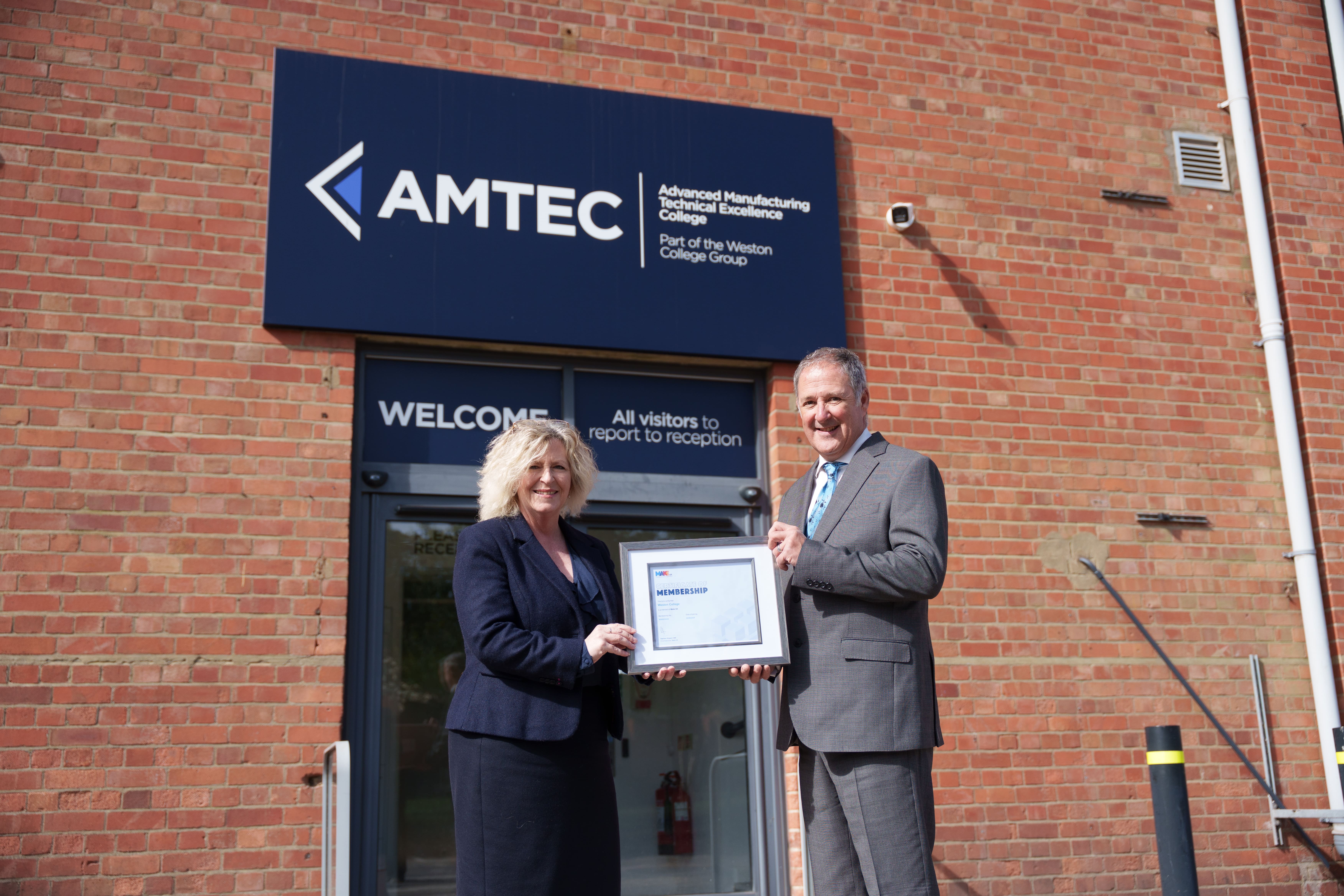 AMTEC sign outside a brick building, with two people holding a membership certificate.