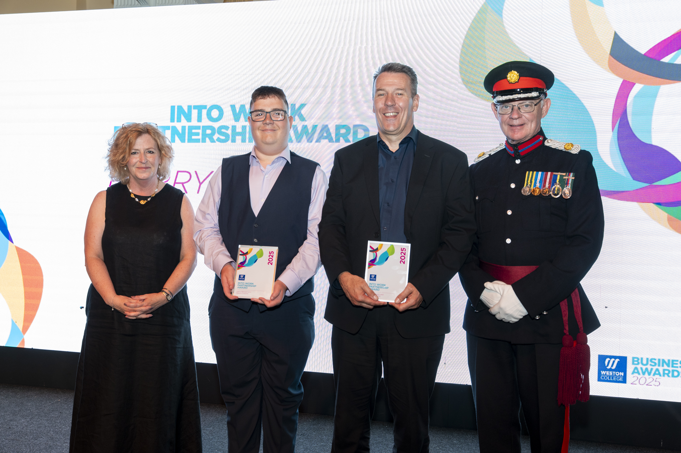 Harry, standing on stage with his employer, and principle Pat Jones being presented the award and posing for a picture