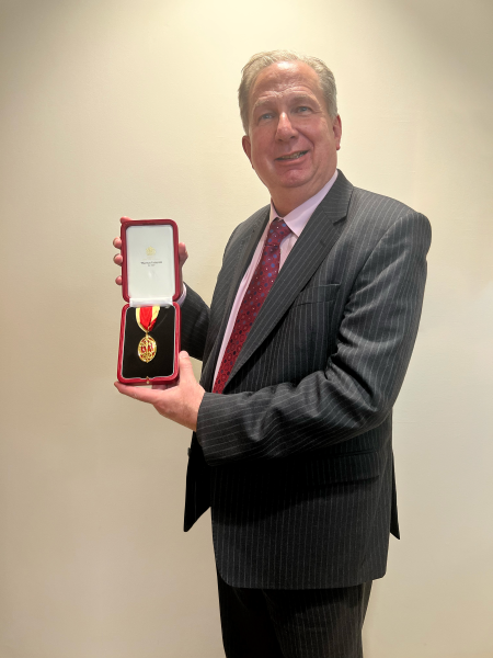 Sir Paul Phillips holding his Knighthood whilst smiling