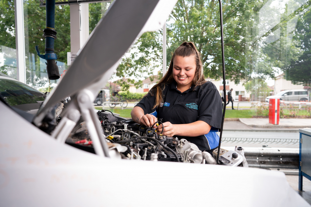 a girl works under the bonnet of a car 