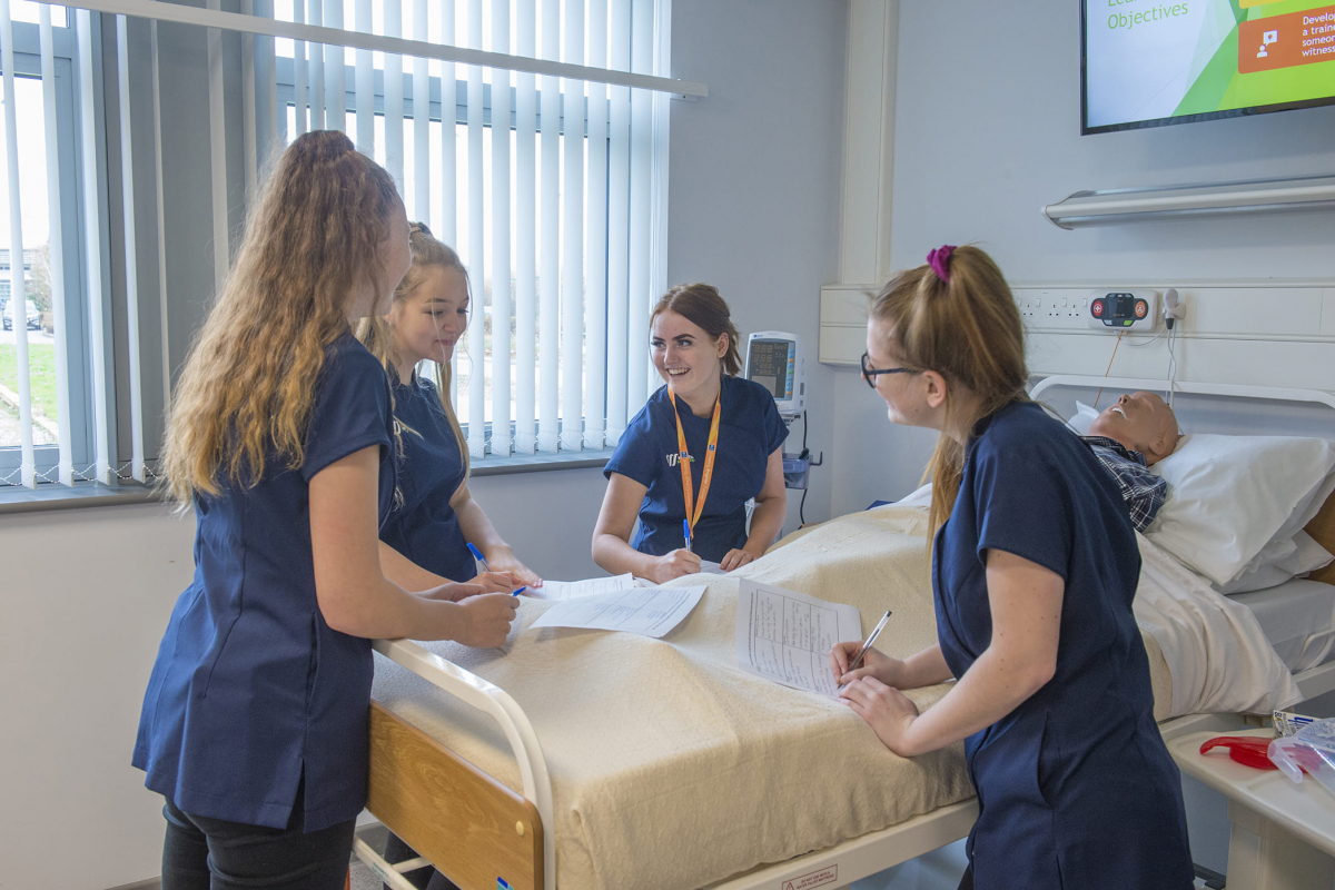 students gather round practice hospital bed
