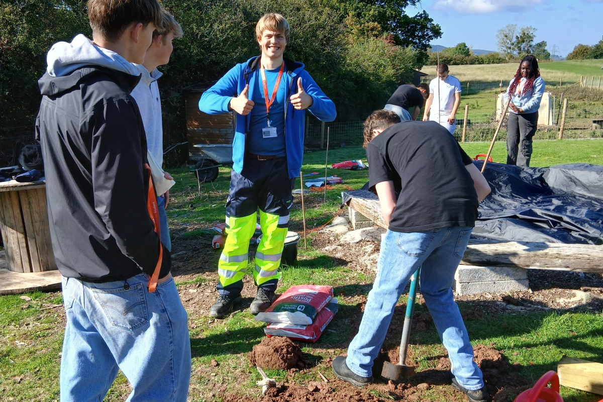 Students digging holes and one student putting their thumbs up 