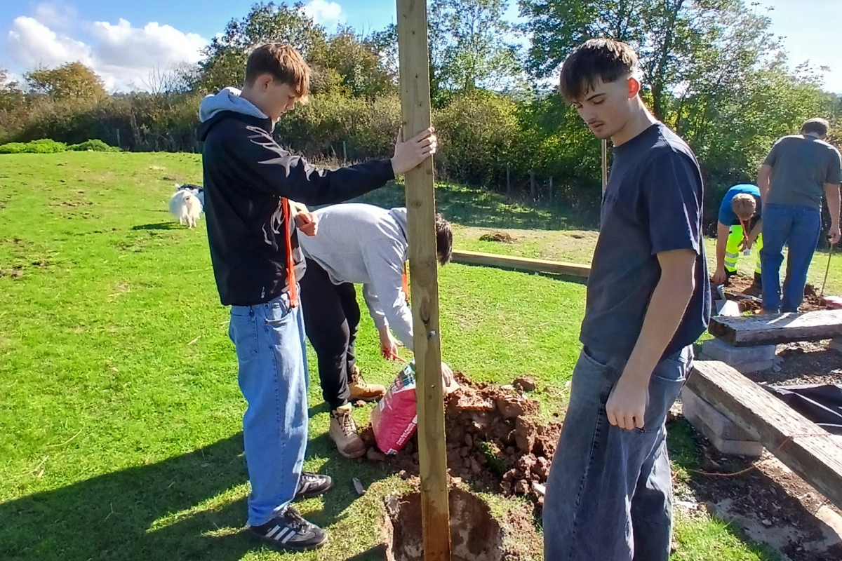 Student holding the wooden post upright in the ground 