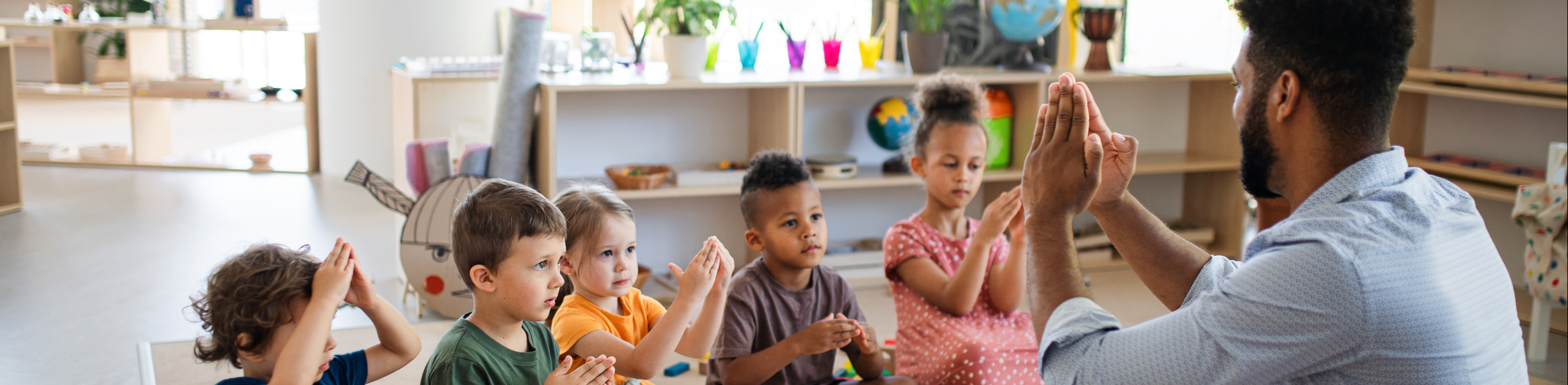 Nursery school children with man teacher sitting on floor indoors in classroom, playing