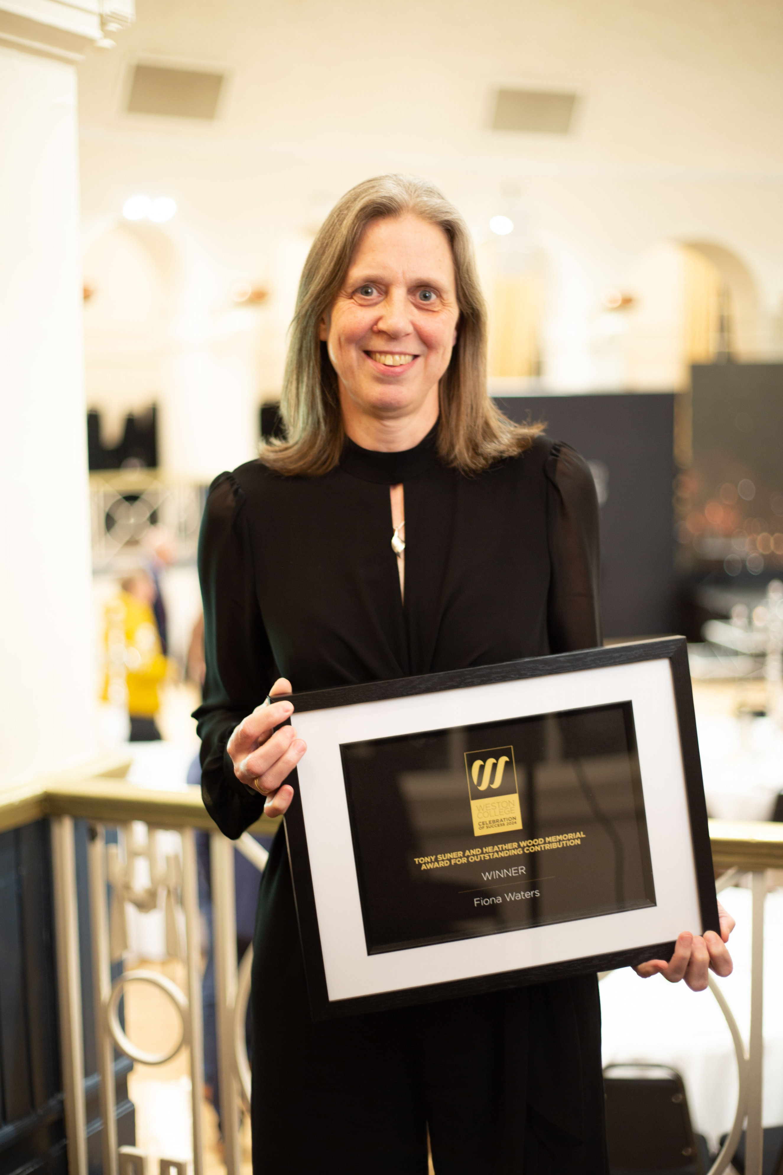 Fiona smiling at the camera on stage whilst holding her award