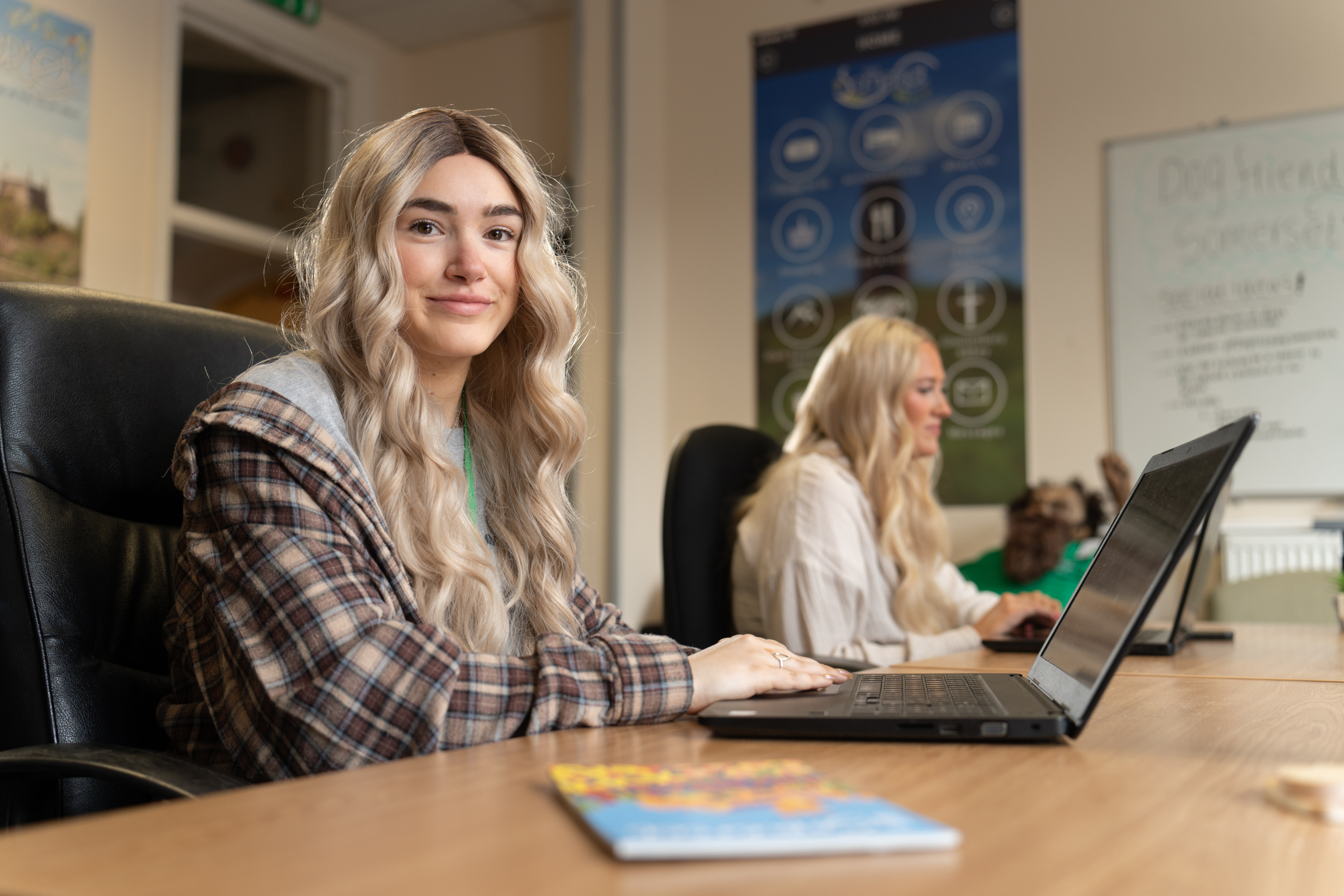 an apprentice smiling while sitting at a desk looking away from her laptop