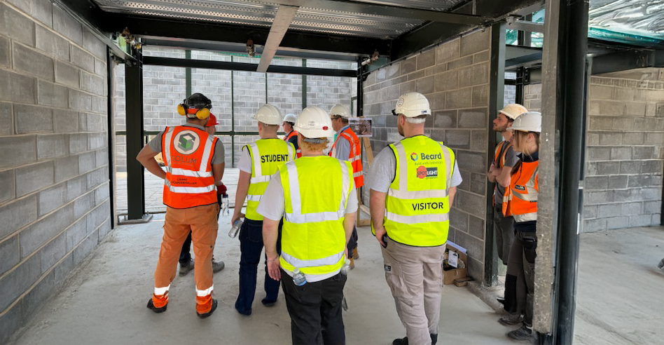 Construction students with high vis' and hard hats on listening to professionals on site