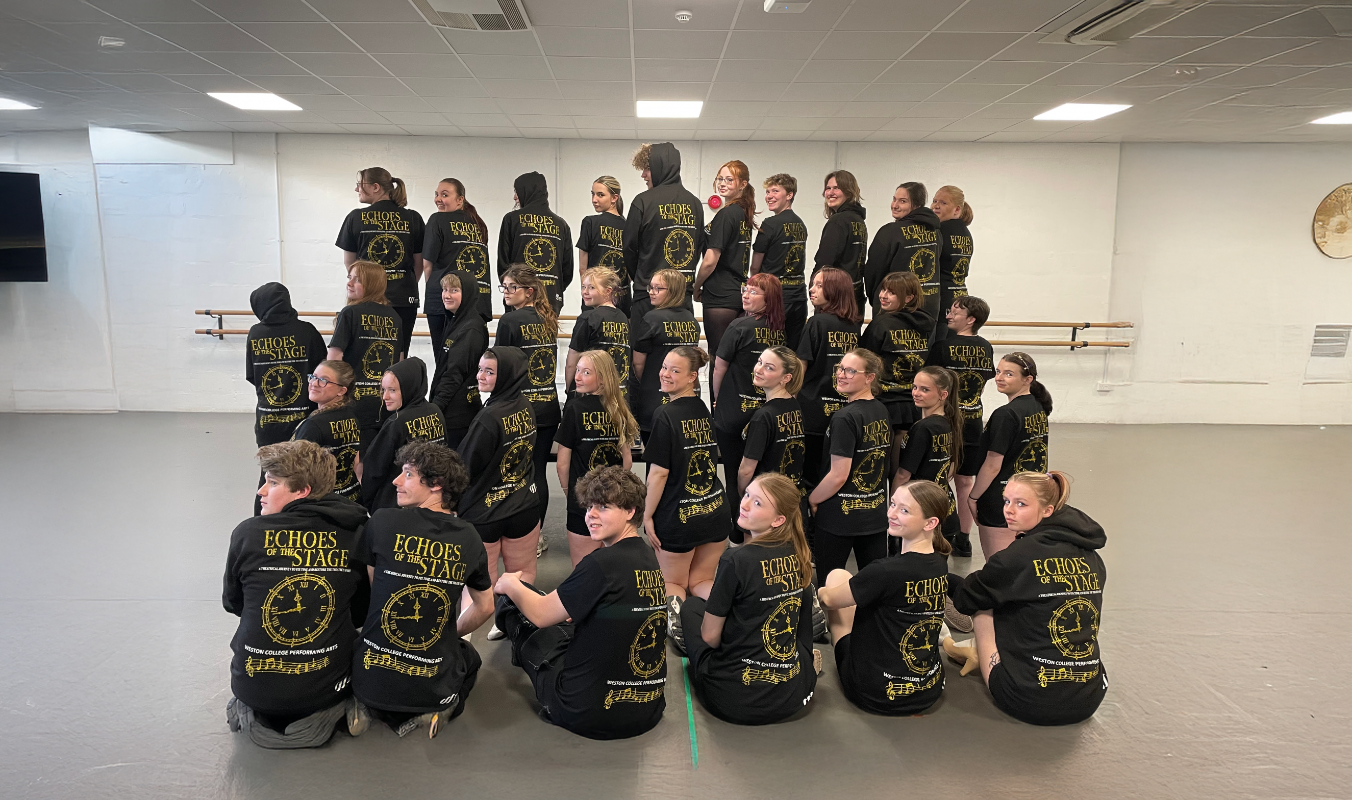 Students wearing 'Echoes of the Stage' t-shirts and hoodies whilst smiling over their shoulders
