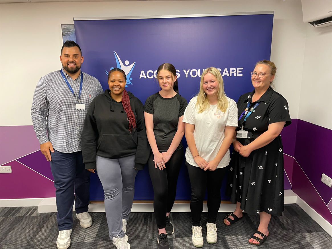 3 students, Caitlin their lecturer, and the CEO of Access Your Care in front of an Access Your Care banner