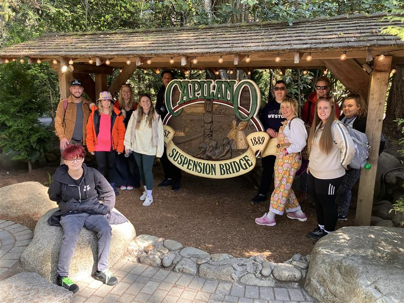 Students and staff standing next to the Capilano Suspension Bridge sign