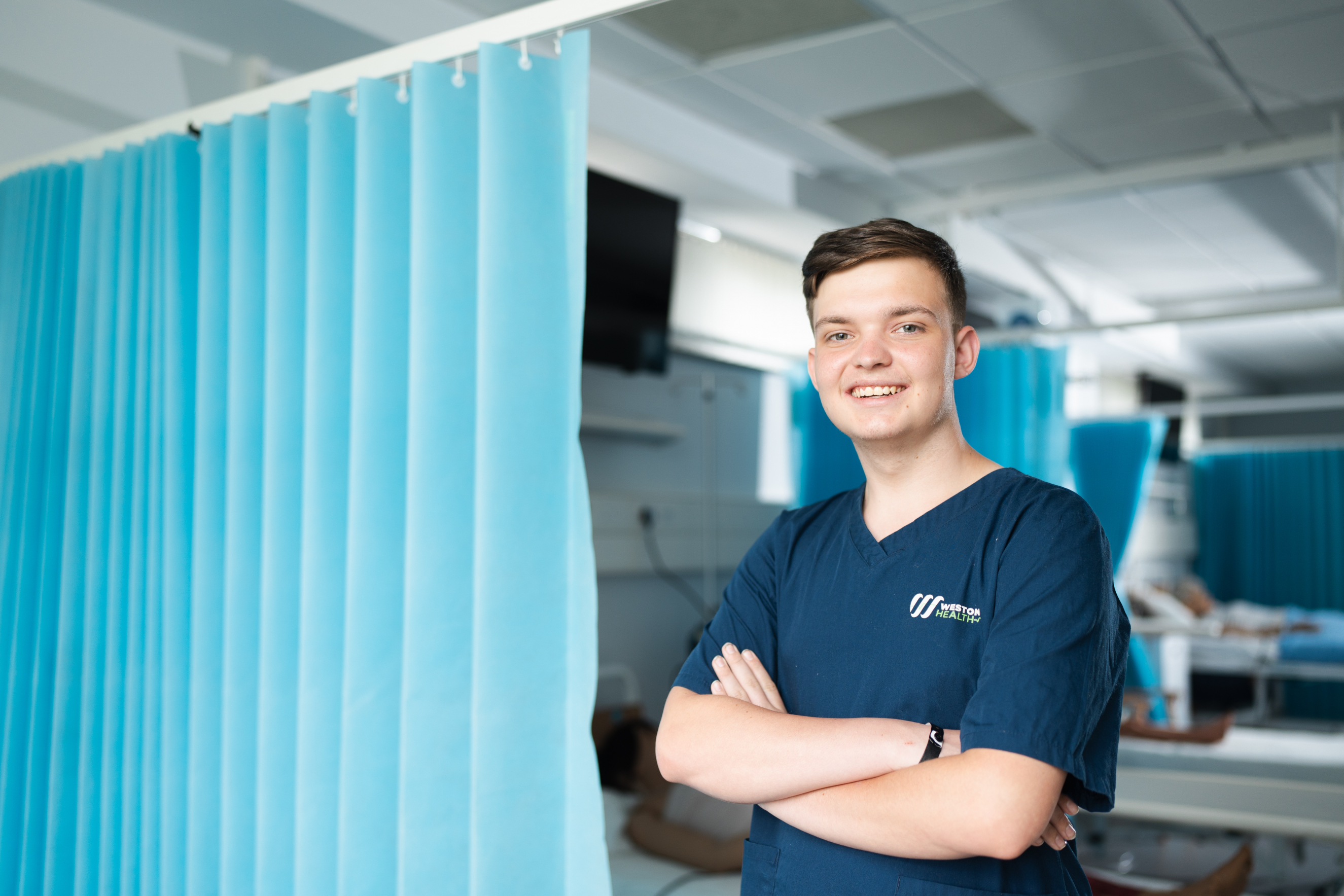 Health student wearing scrubs whilst smiling in the Simulation lab