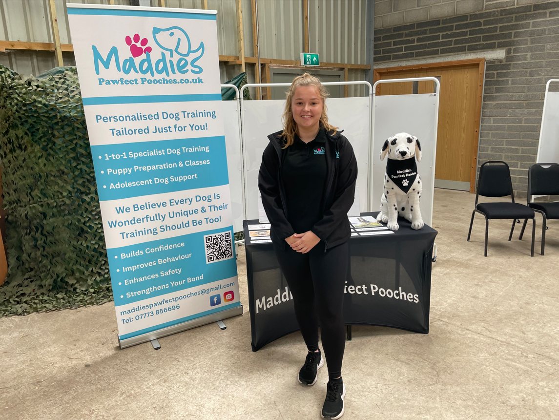Maddie standing next to her Maddie's Pawfect Pooches banner and stand