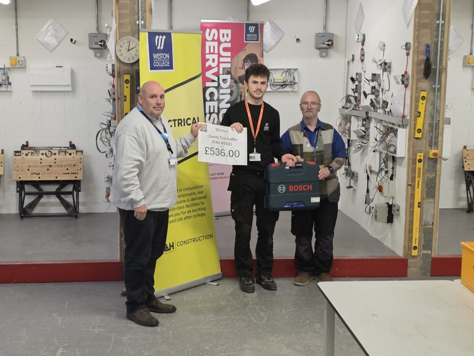 Head of Construction, Richard Hanney, lecturer, Neil Adams, and winner of the raffle smiling for a photo with the Bosch Drill