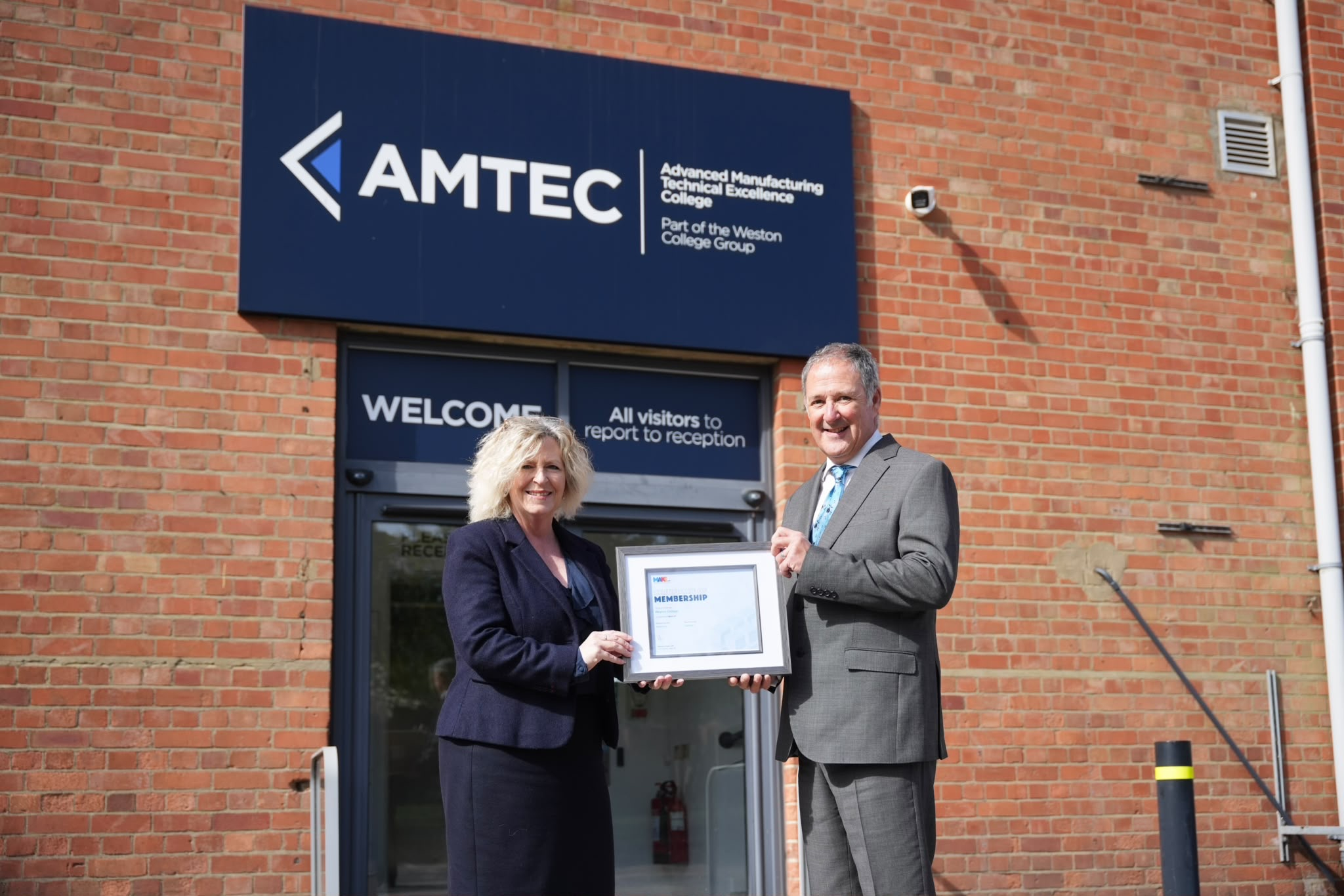 Principal Pat Jones and Jim Davison from Make UK Posing for photo in front of AMTEC building
