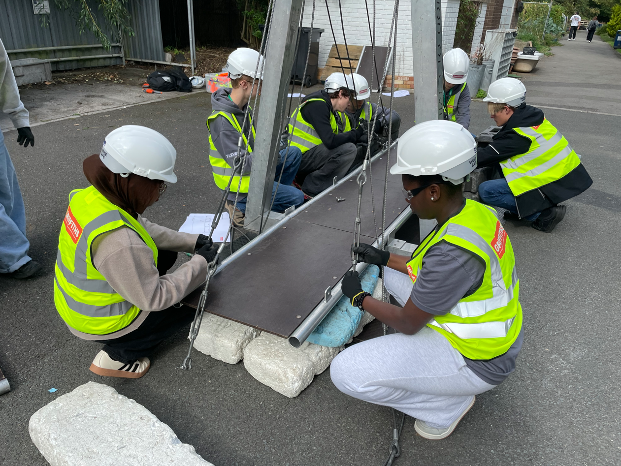 Students building a bridge with hi-vis and hard hats on