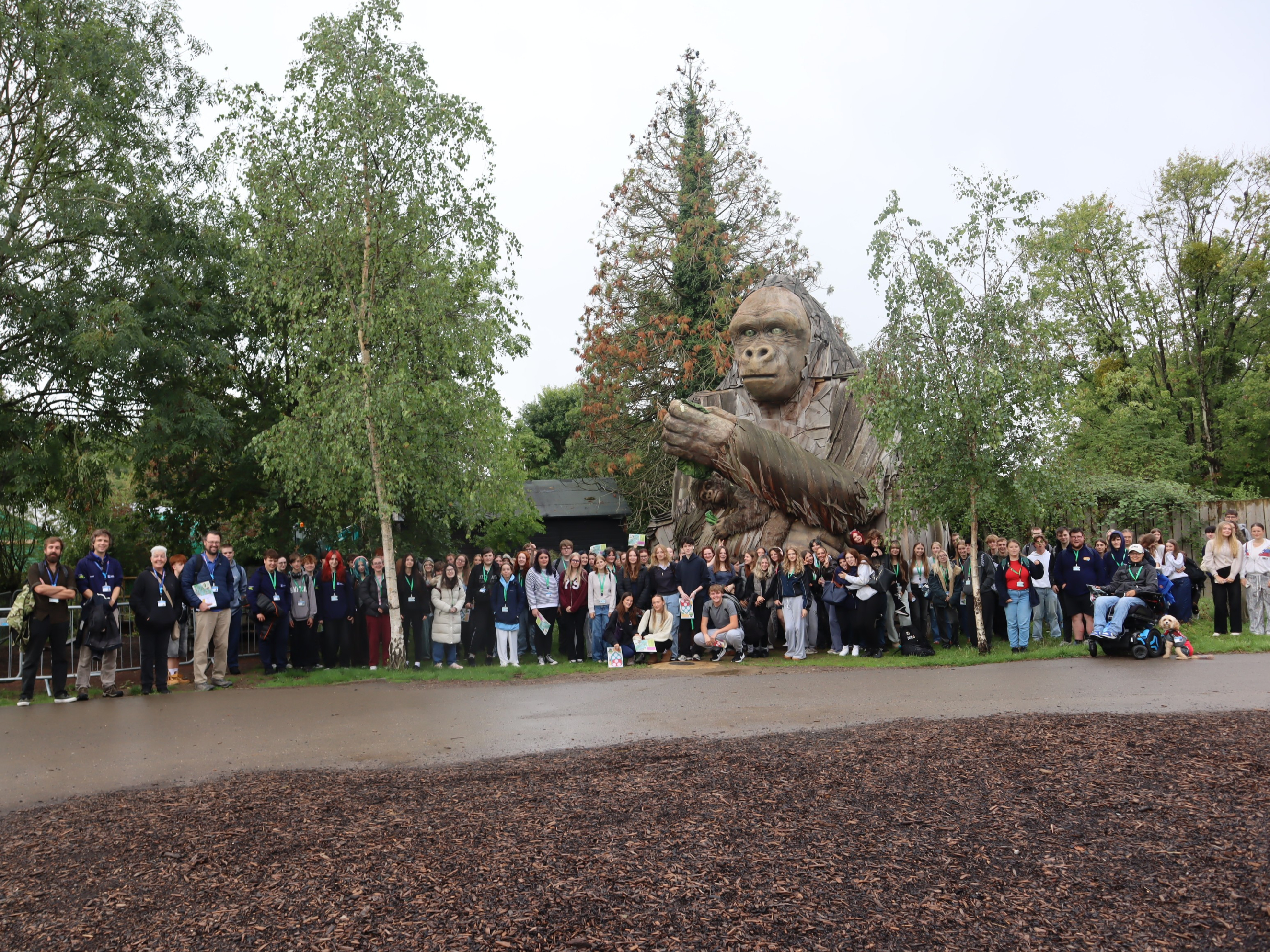 Group photo of animal students by a large wooden monkey statue