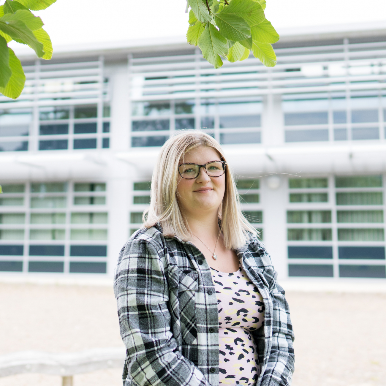 Female student with blonde shoulder length hair wearing glasses a plaid shirt stood underneath a tree at Weston College's Loxton Campus
