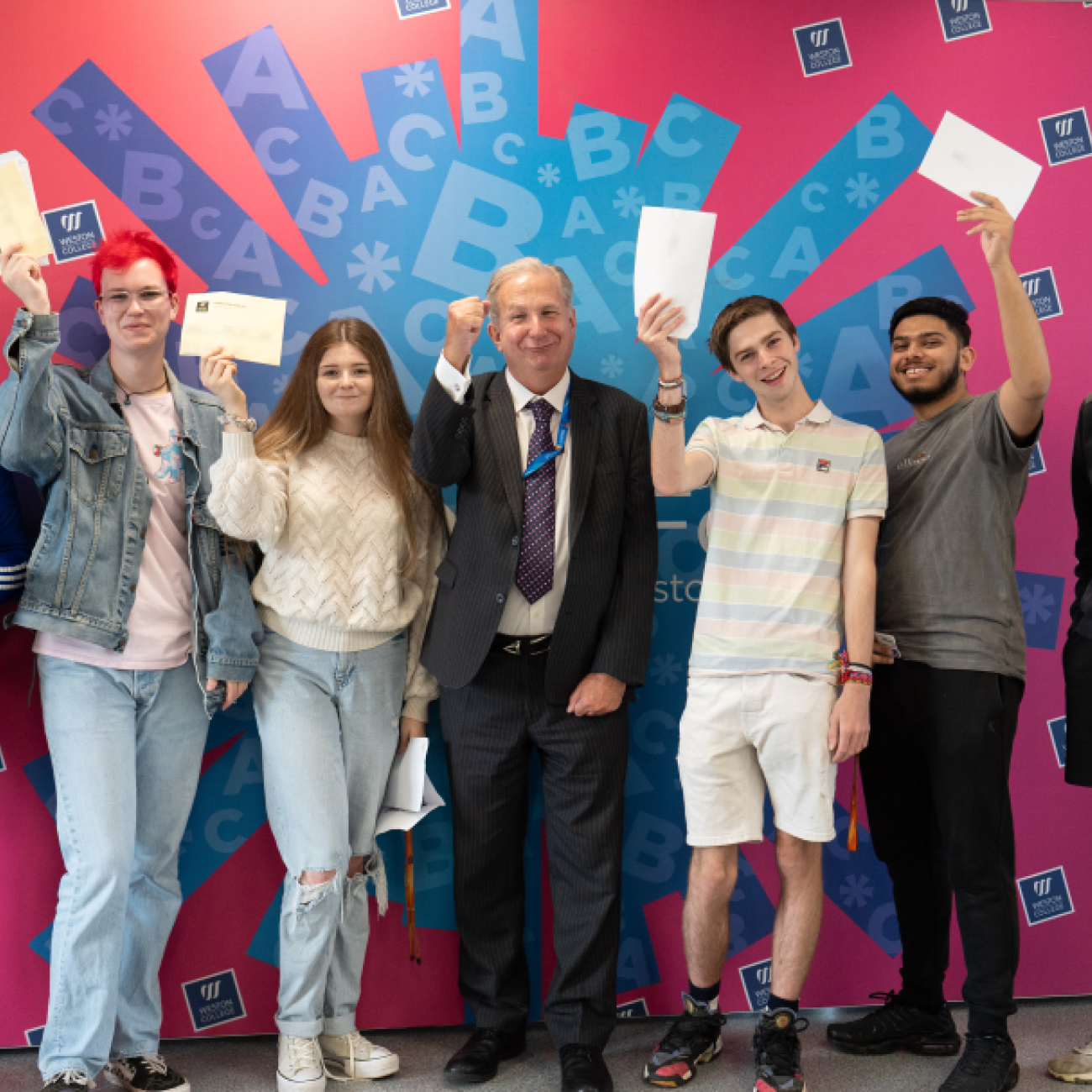 Learners Celebrating their A Level Results, holding up their papers with Sir Paul Phillips stood in the middle. 