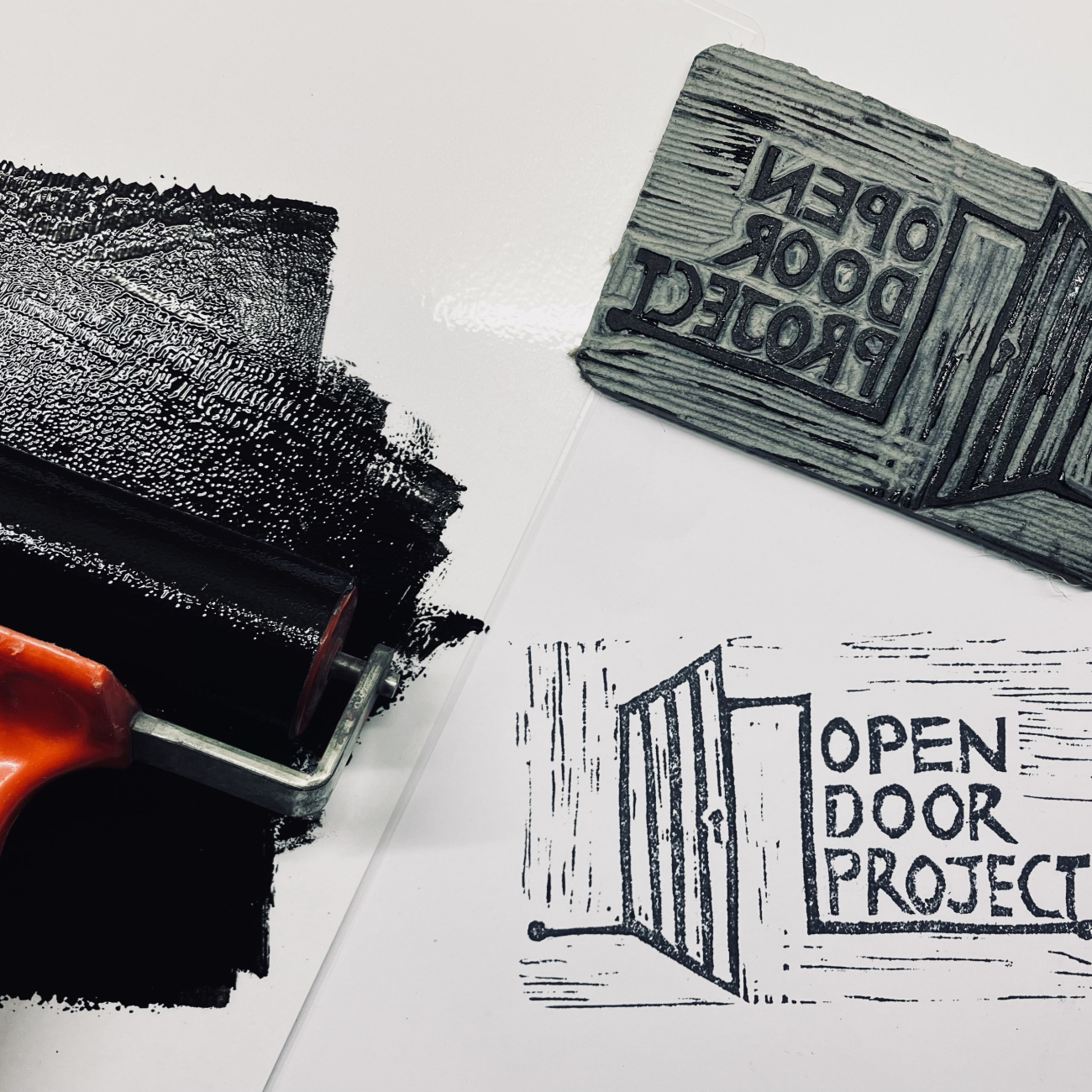 Painting a wall black using a roller, with the words 'Open Door Project' on the side