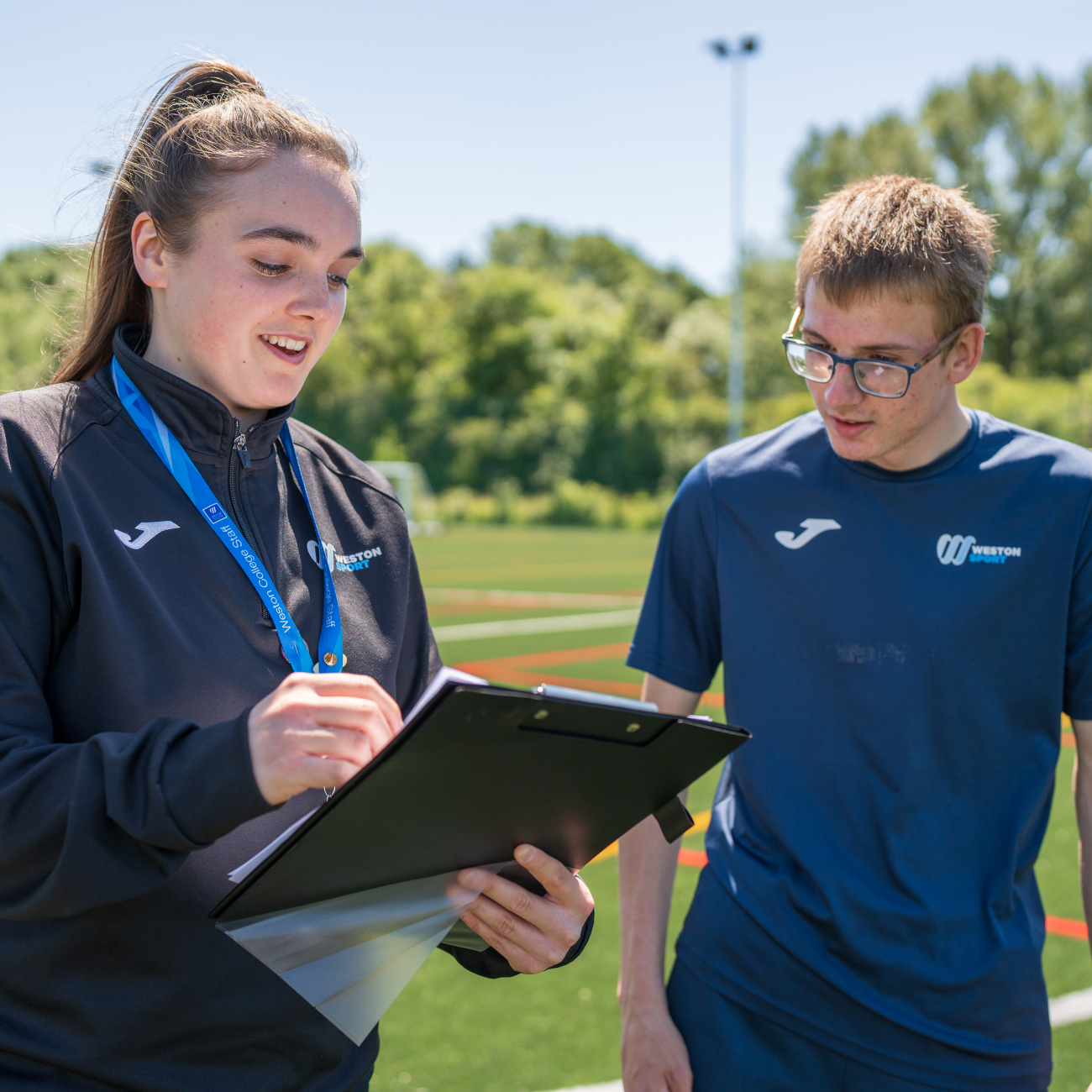 A Weston College sport lecturer on the sports field with a student both looking at a clipboard