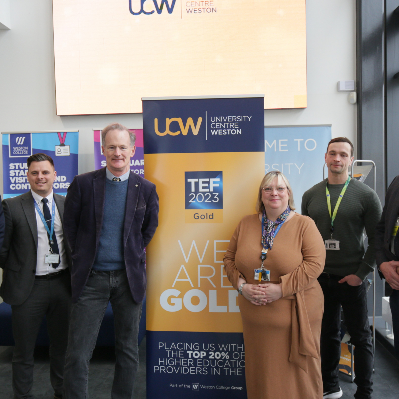 John Penrose, Andrew Leighton-Price and others stand by a sign saying UCW 'TEF Gold'