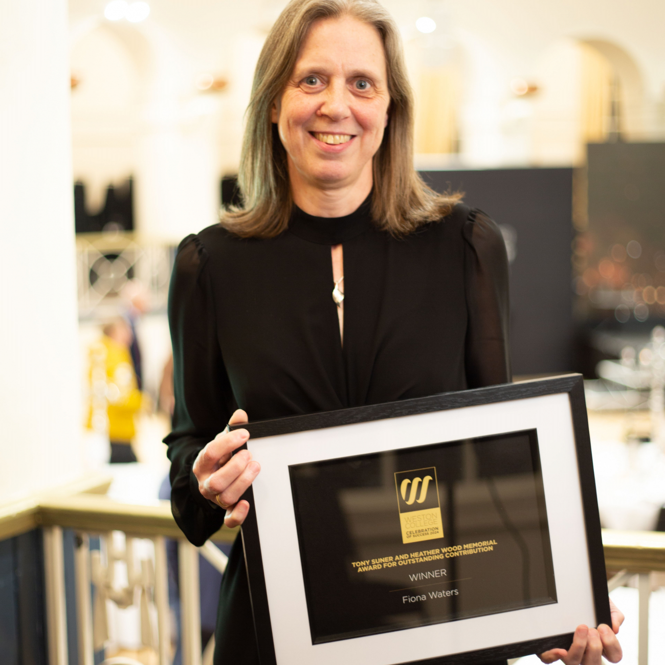 Fiona smiling at the camera on stage whilst holding her award
