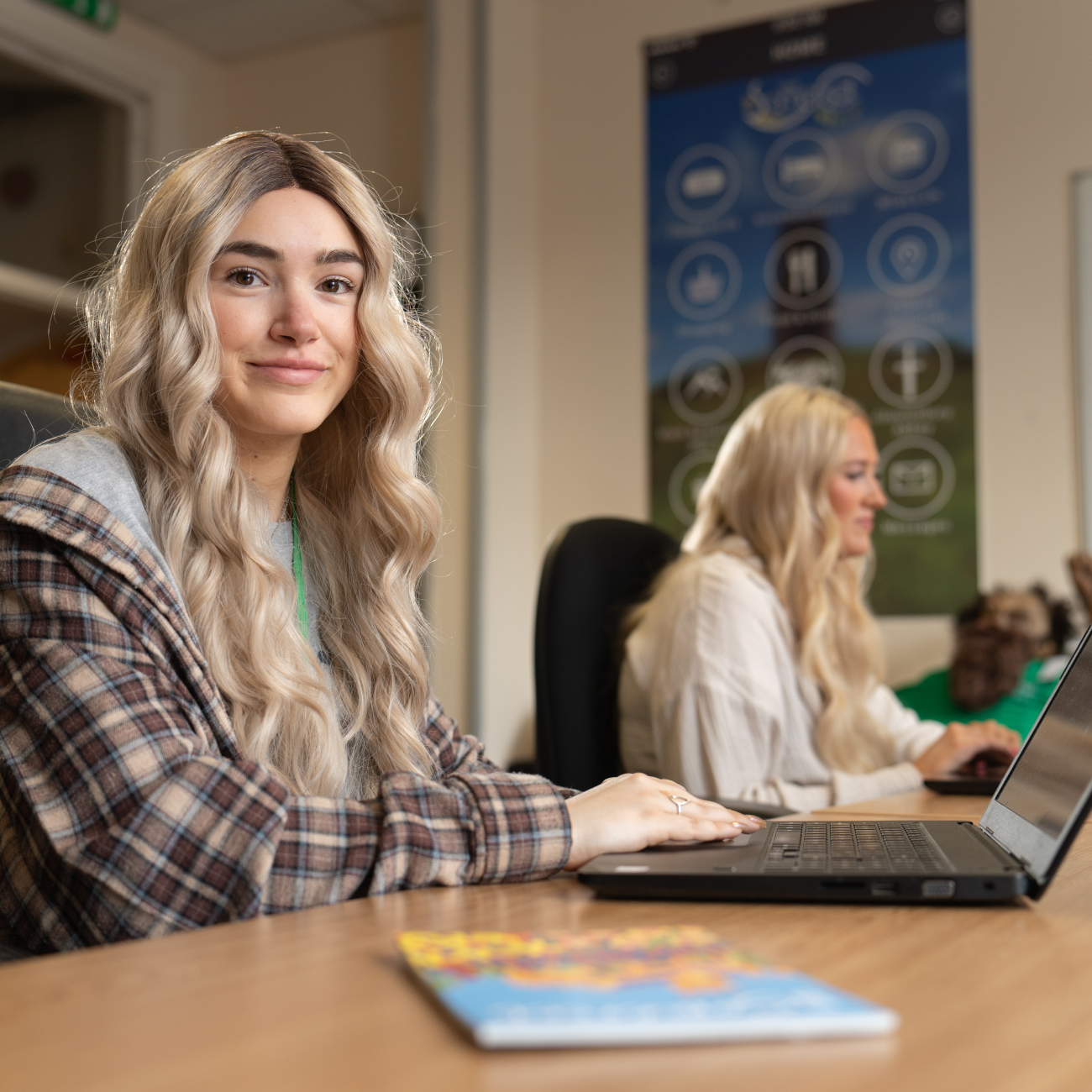 an apprentice smiling while sitting at a desk looking away from her laptop