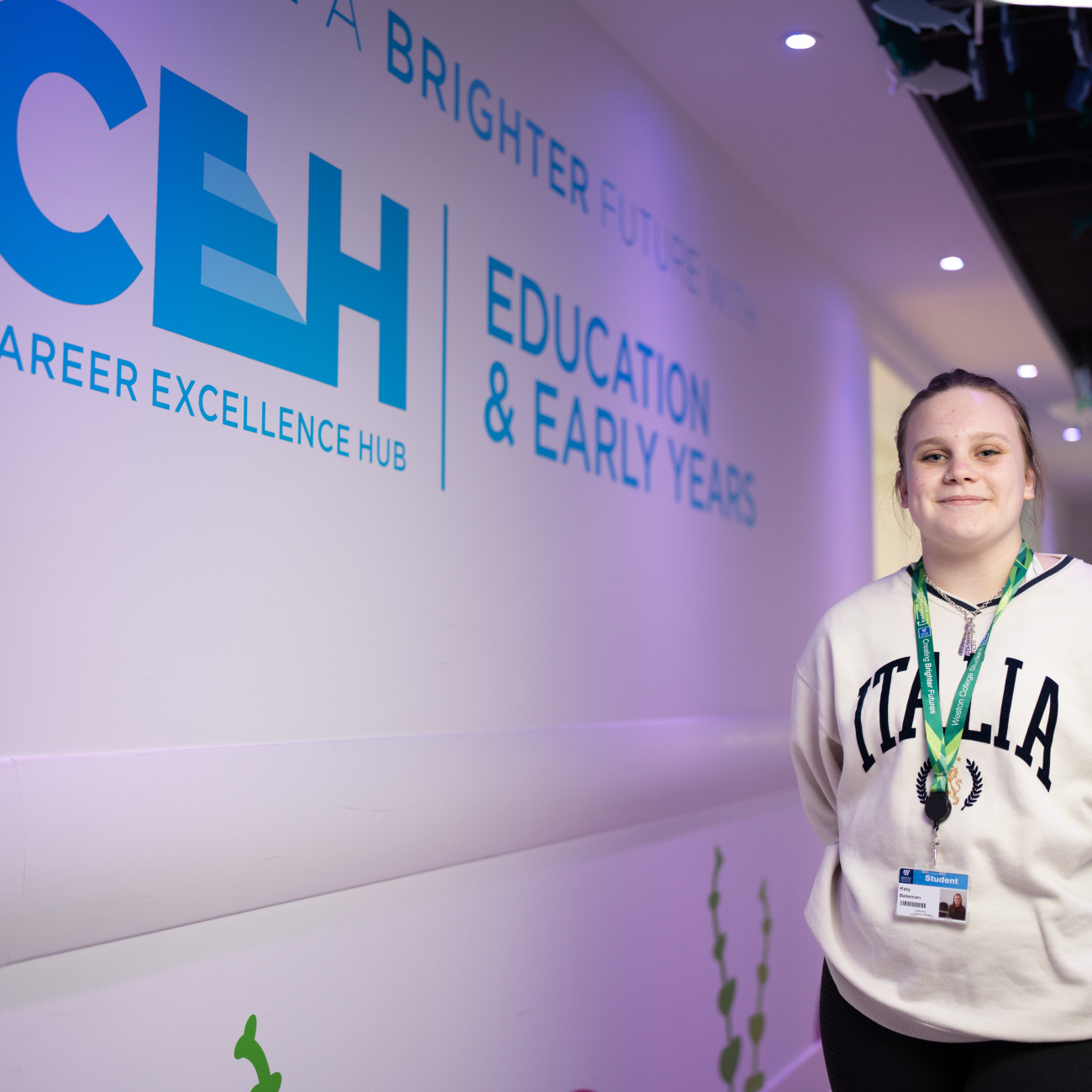 Katy from Early Years standing smiling by the Early Years sign