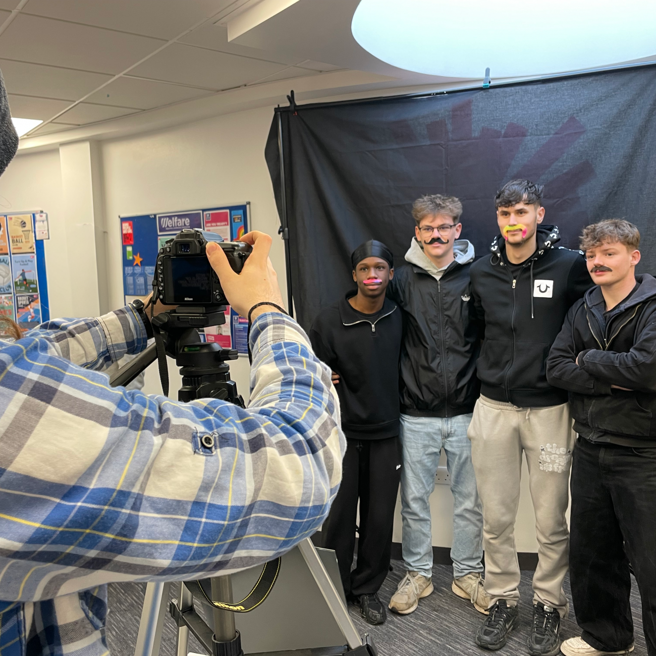Students smiling with moustaches on in front of the camera