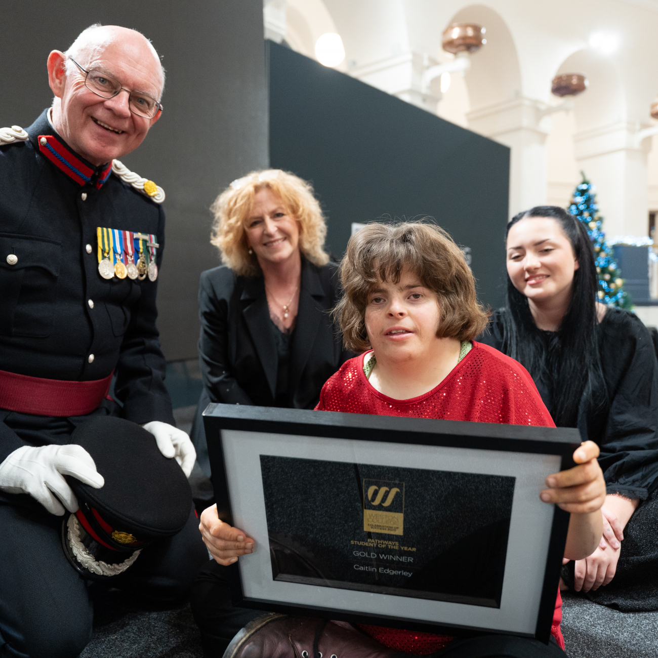 Caitlin on stage holding her award next to Brigadier Nigel Beacom