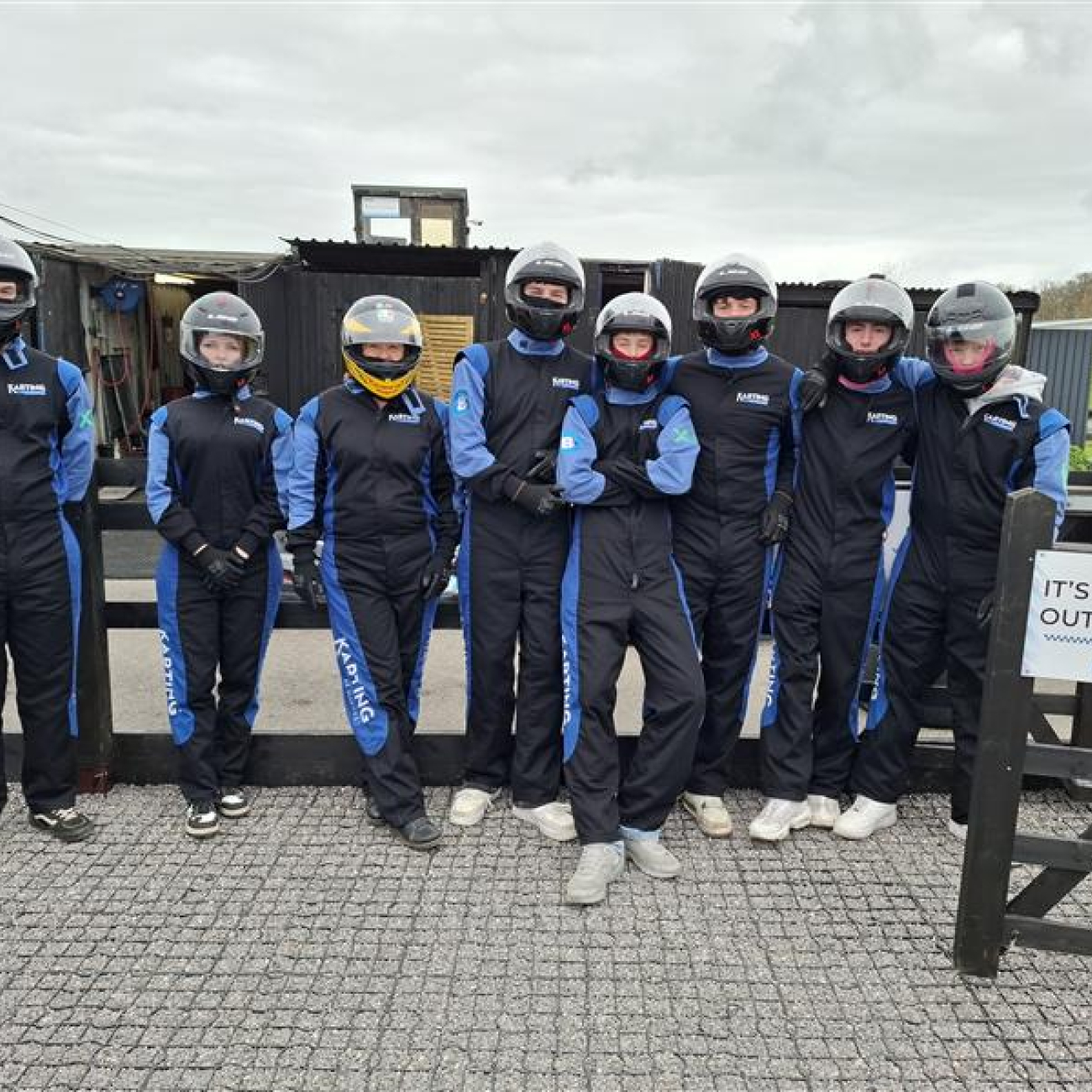 Students standing wearing their go-karting uniforms in front of the track