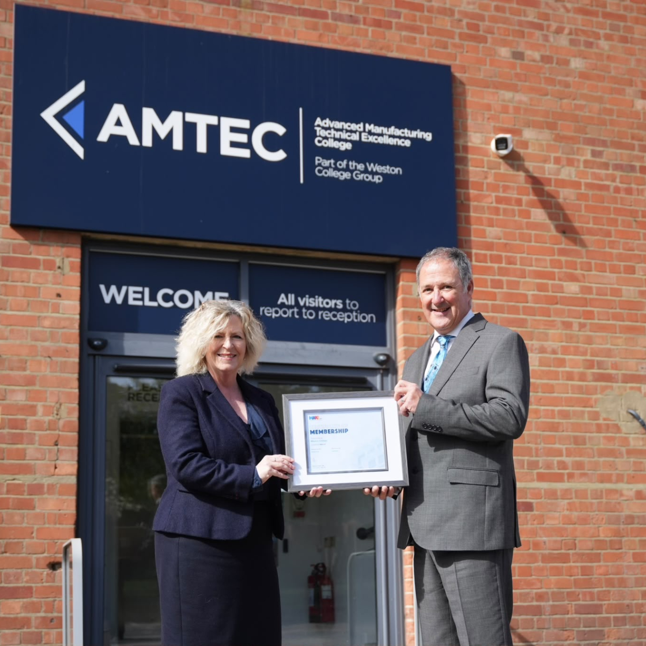 Principal Pat Jones and Jim Davison from Make UK Posing for photo in front of AMTEC building