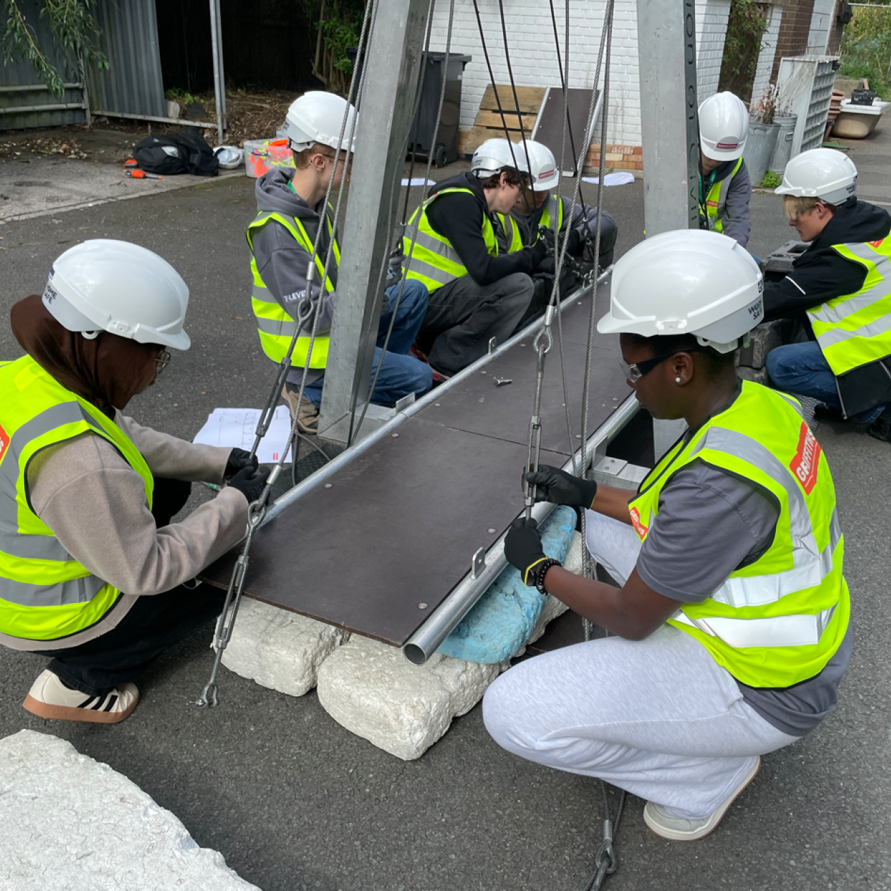 Students building a bridge with hi-vis and hard hats on