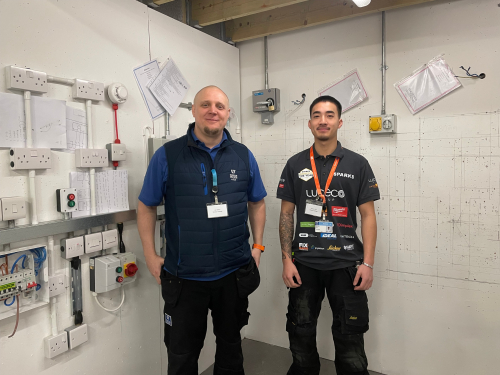 Marcus and lecturer, Lee, standing smiling in the practice workshop