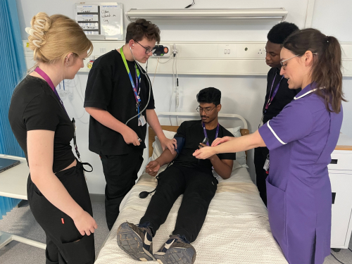 Health and Social Care learners manually checking their classmates blood pressure using a stethoscope and blood pressure reader
