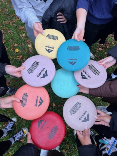 Students holding together a range of coloured frisbees