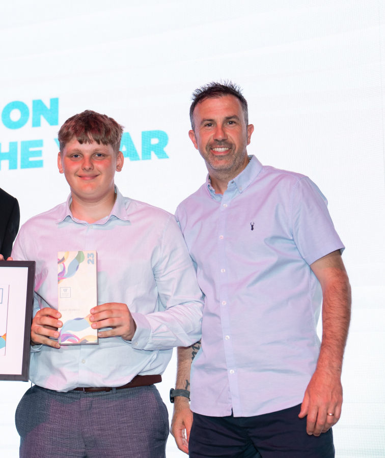 kash standing with his awards on stage alongside two men