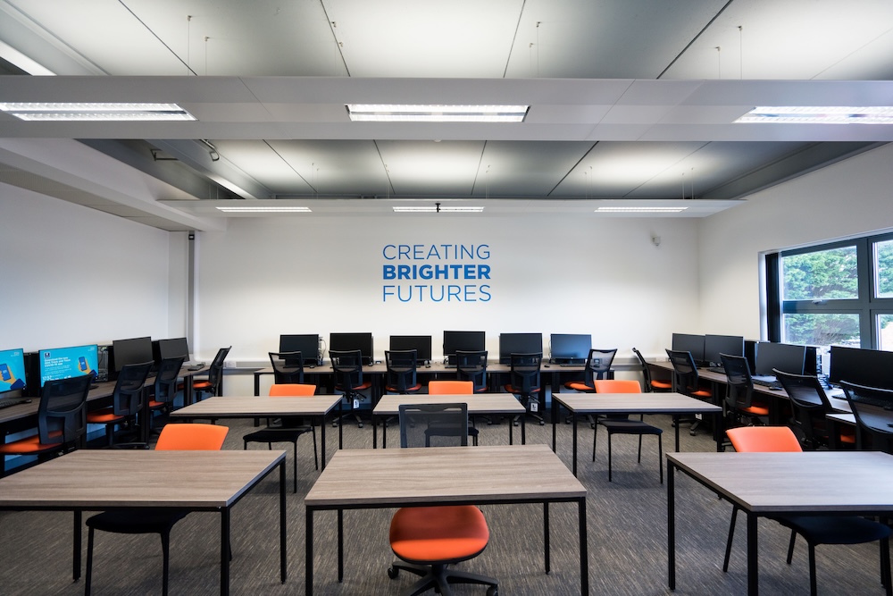A classrooom with computers around the edge and desks in the middle, decked in WEIOT orange