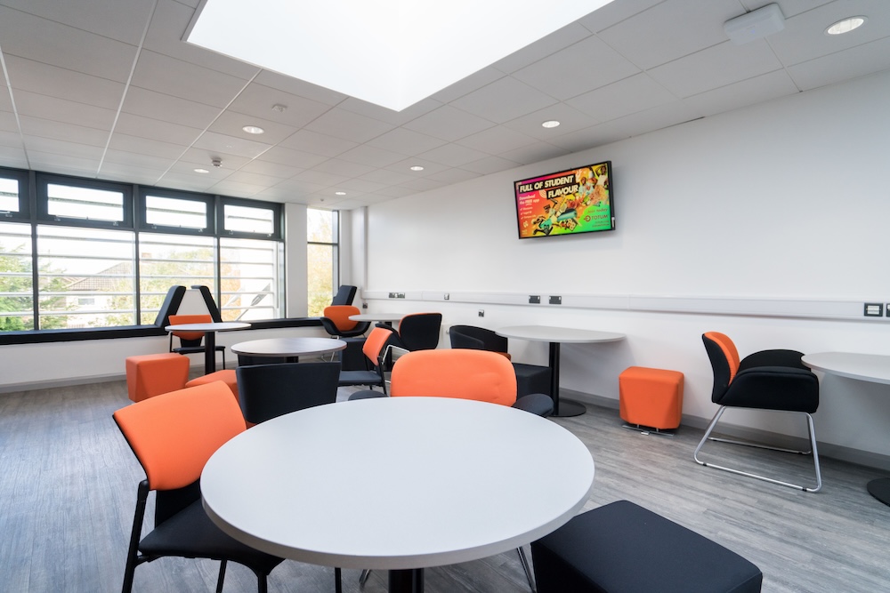 Communal area at WEIOT with table and chairs decked out in WEIOT orange and black, also a tv is on the wall